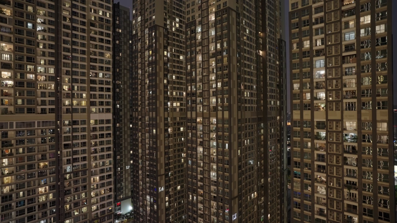 Towering Apartment Buildings At Night In Ho Chi Minh, Vietnam, With Repetitive Grid Of Illuminated Windows Against Dark Sky. elevated, static shot