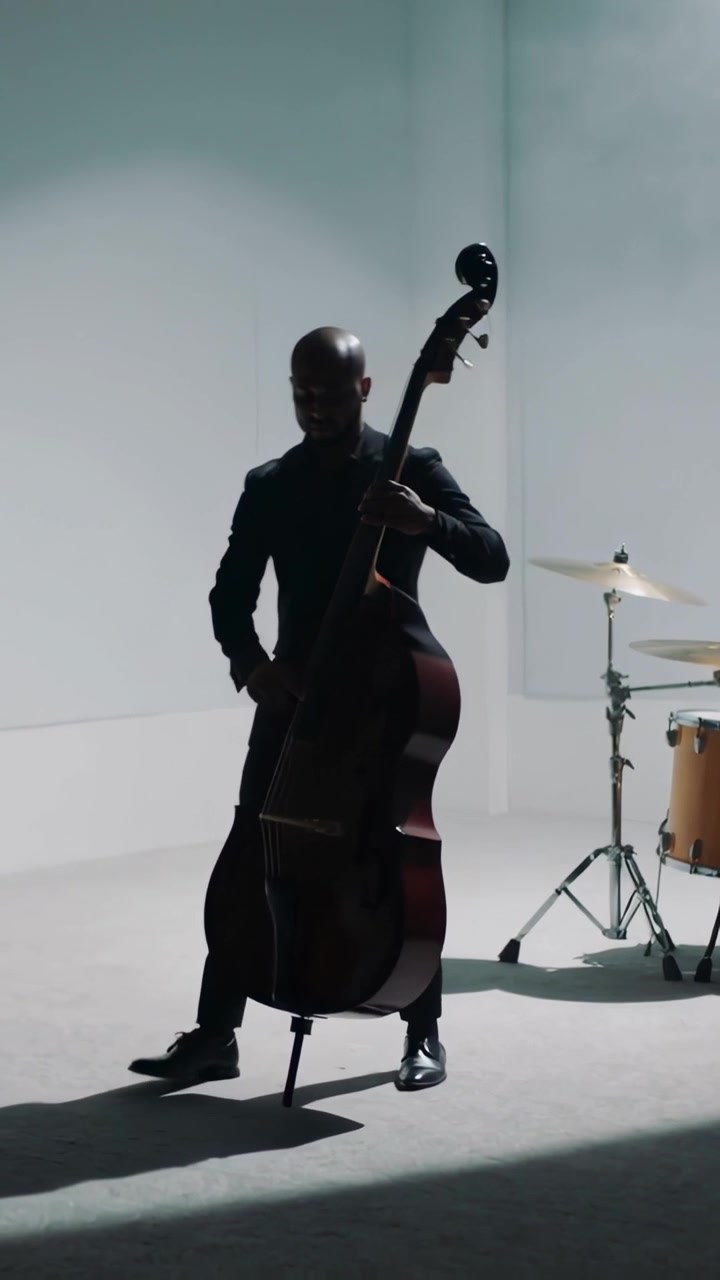 Video verticale: Suonando il contrabbasso in uno studio bianco, il bassista in abito si aggiusta, seguendo il piatto