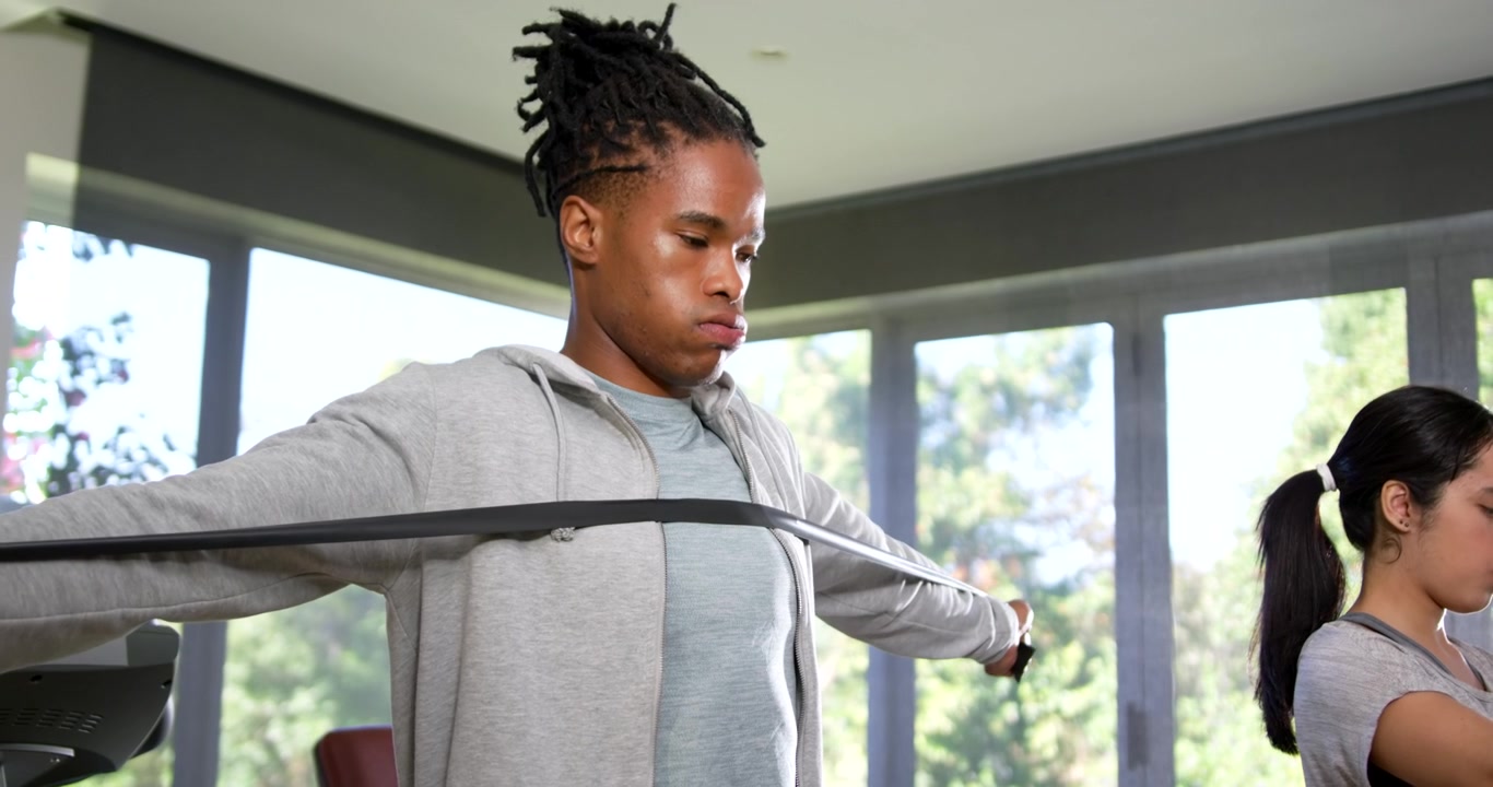African American workout partners holding band in bright gym, pulling outward, building strength