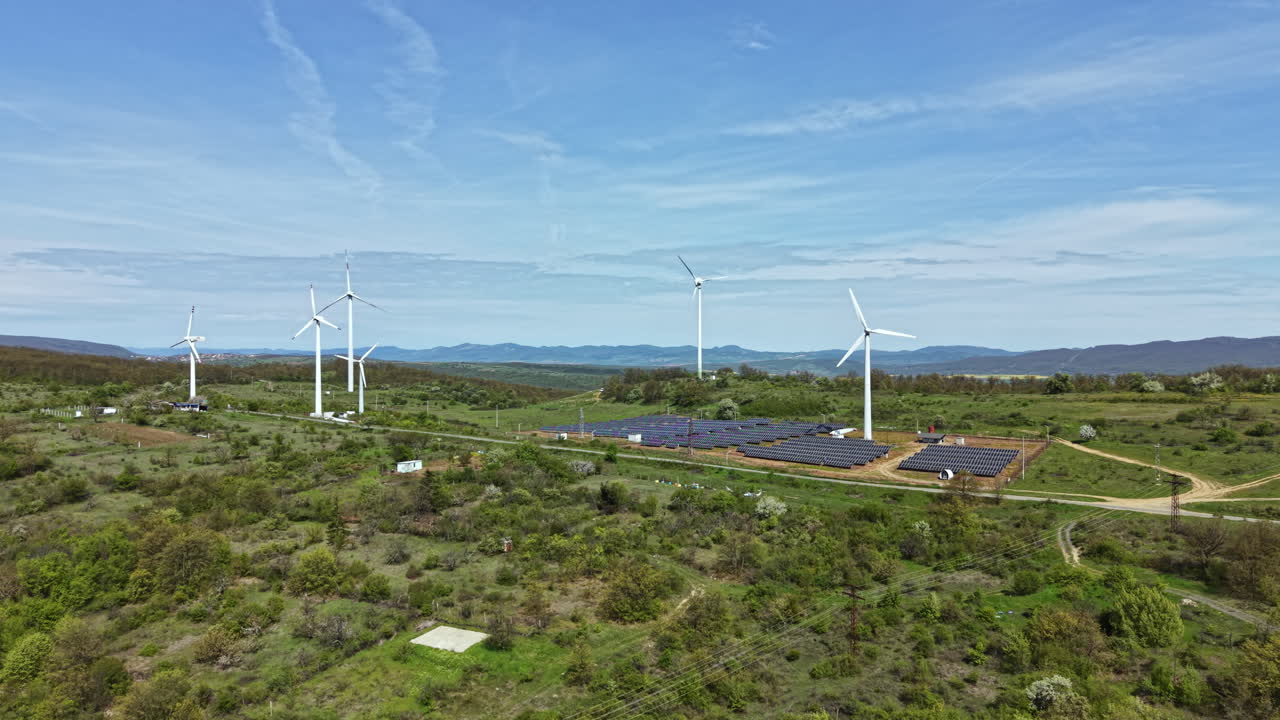 Turbinas eólicas e painéis solares trabalham juntos em uma fazenda de energia renovável em uma paisagem verde sob um céu claro durante o dia.