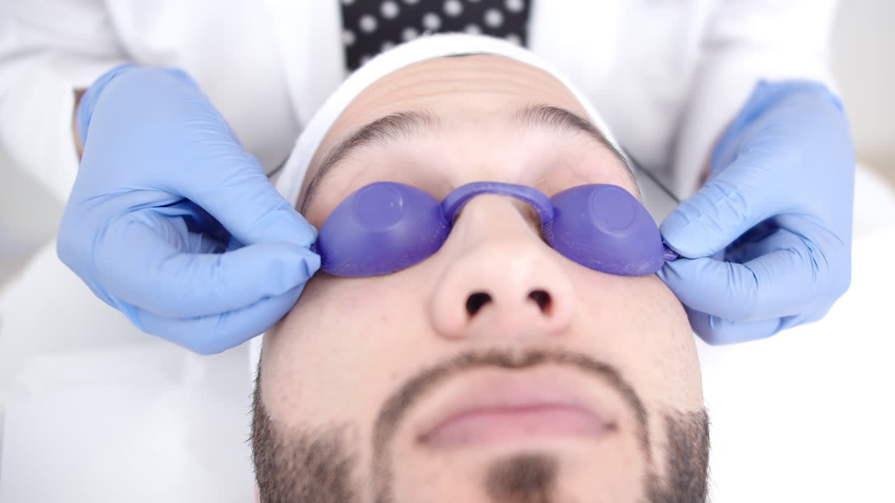 Amazing close-up shot of a handsome young man lying on a stretcher while the female doctor puts eye shield on him for beauty treatment