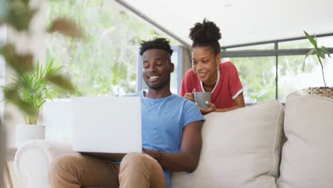 Video-De-Una-Feliz-Pareja-Afroamericana-En-Un-Sofá-Con-Café-Y-Una-Computadora-Portátil