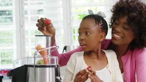 mother and daughter putting strawberries in juicer