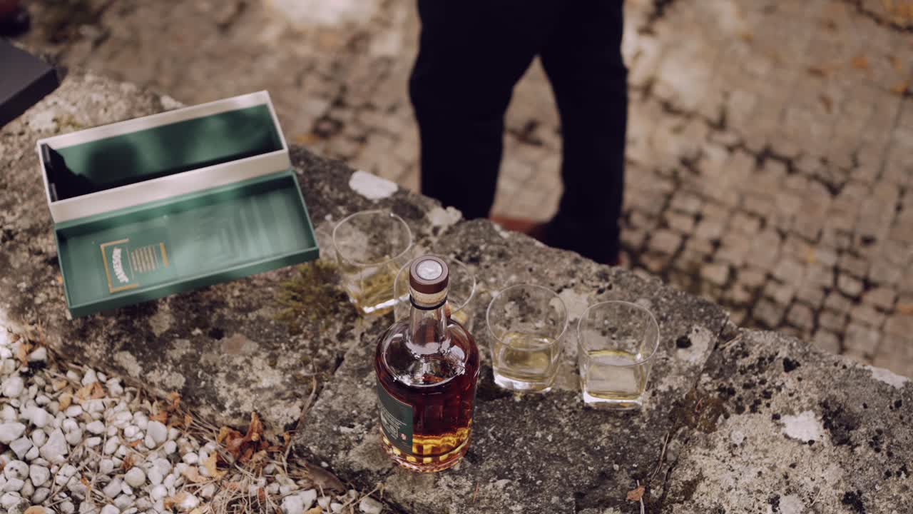 Man serving whiskey into glasses on a rustic outdoor stone table.