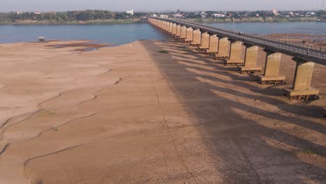 Licht-Am-Frühen-Morgen-Wirft-Schatten-Auf-Eine-Sonnenbeschienene-Brücke,-Während-Sandbänke-Auf-Dem-Mekong-Freigelegt-Werden,-Wenn-Der-Wasserspiegel-Aufgrund-Vorgelagerter-Dämme-Sinkt