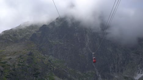 tiny red gondola slowly passes between mountain peaks into the clouds