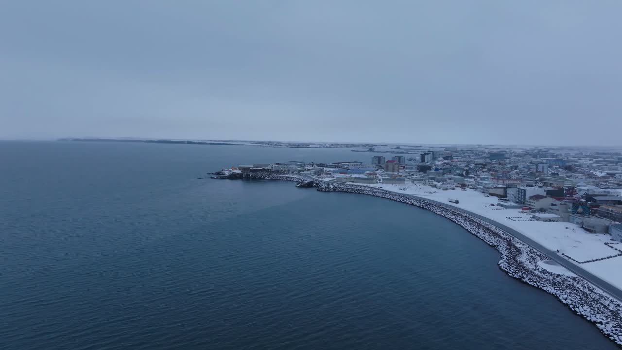 Luftpanorama av Keflavik bys kystlinje og havet i et islandsk vinterlandskap.