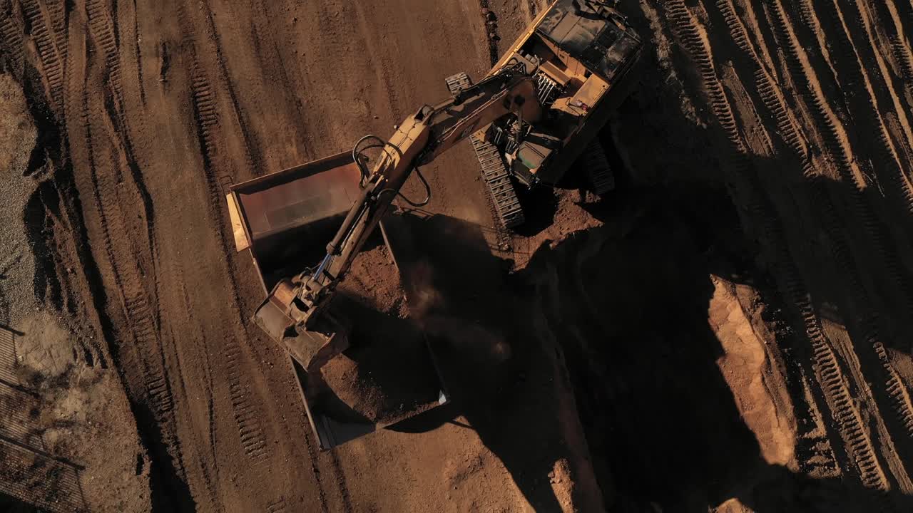 una excavadora aérea cargando un camión de basura con tierra en un sitio de construcción