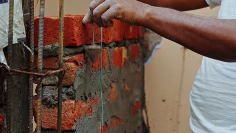 indian-labor-in-construction-site-making-manual-Plumb-Bob-measurement-calculating-distance-from-the-brick-wall