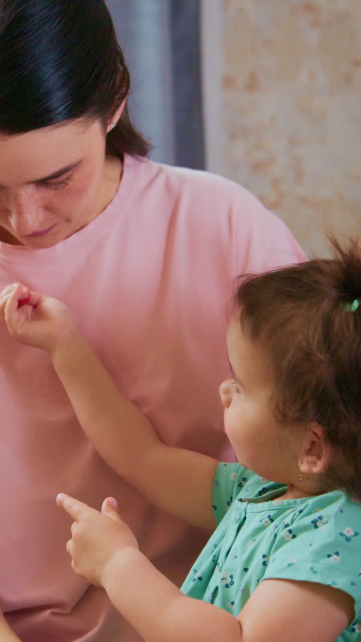 A Caring Moment: Mother Gently Styling Her Child's Hair, Creating Beautiful Pigtails While Sharing Joyful Smiles and Bonds in a Cozy Indoor Setting