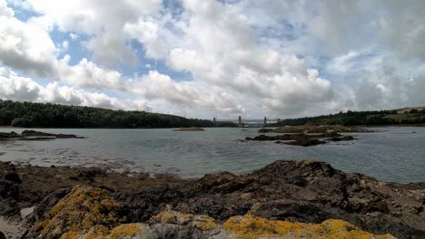 Estrecho-De-Menai-Galés-Rocoso-Lapso-De-Tiempo-Cruce-De-Transporte-Del-Puente-Britania-Con-Nubes-Que-Pasan-Por-Encima