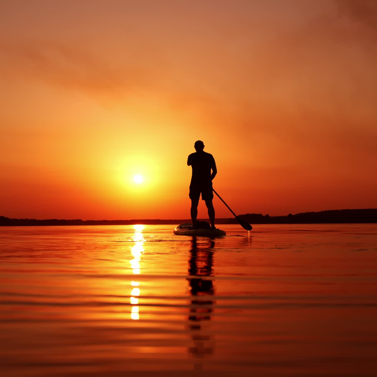 Dark male silhouette standing on sup board on the river. Man rowing slowly distancing from the camera