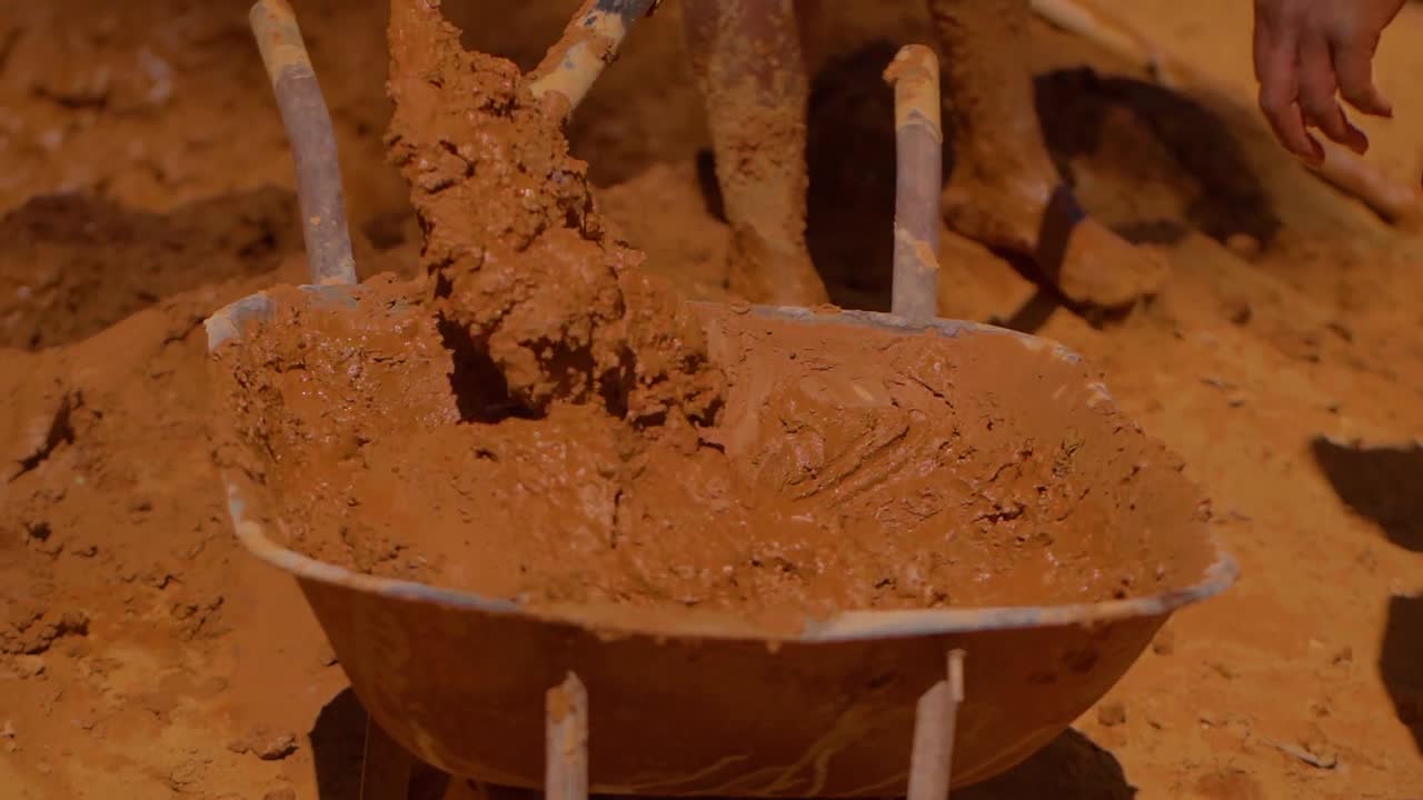 Construction workers mixing mud and clay in a wheelbarrow, employing traditional techniques for adobe brick building in Chapada dos Veadeiros, Brazil