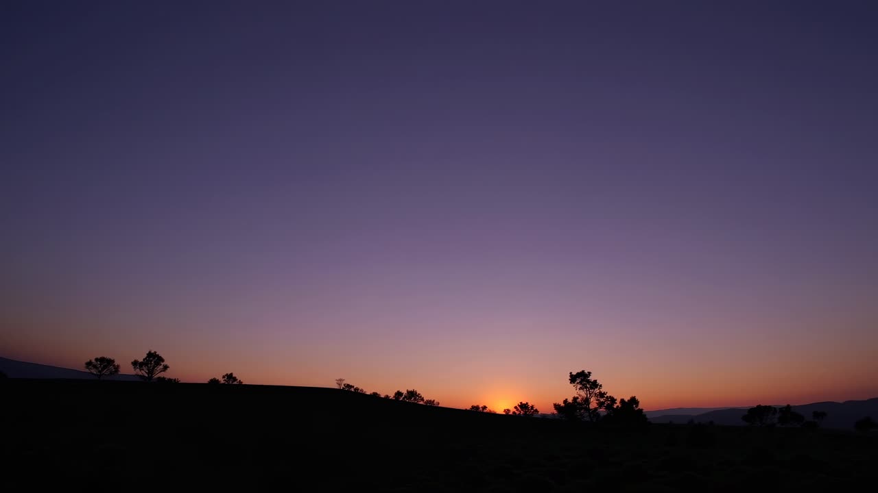 A serene sunset video captures a wide-angle view of a silhouetted landscape, blending vibrant orange