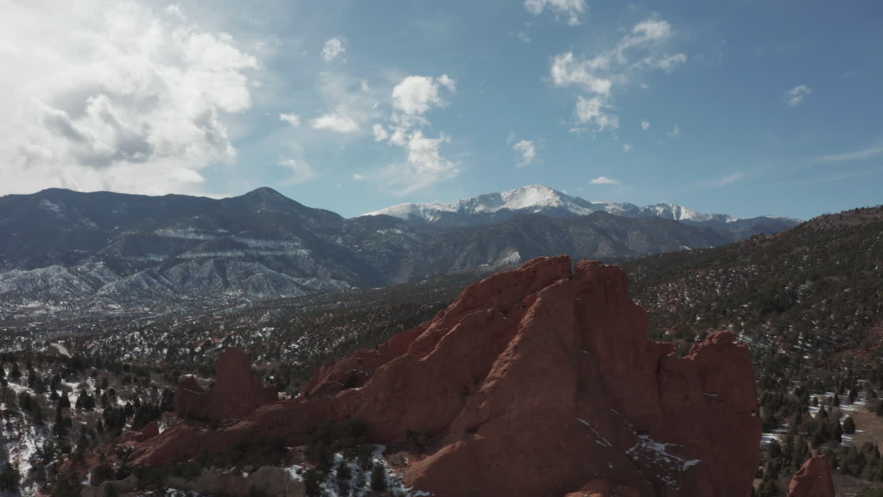 Aerial left to right tracking shot over red rocks, Pikes Peak in background.