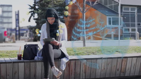 globe and multiple digital icons floating over woman in hijab using digital tablet on the street