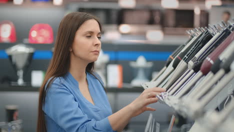 In-the-appliances-store,-a-brunette-woman-in-a-shirt-chooses-a-blender-for-shopping-by-viewing-and-holding-the-device-in-her-hands.