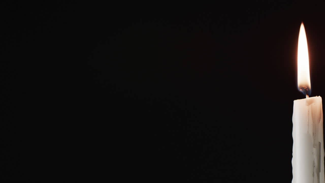 Video of white candle with white flame and copy space on black background