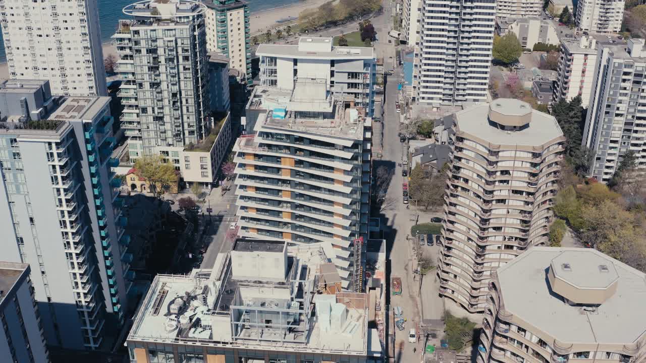 Aerial panout from English Bay, downtown Vancouver, BC, Canada. Sparse outdoor, quiet beaches, roads, and tropical tourist hotspots next to residential and commercial towers.