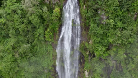 paneo aéreo a la derecha de la cascada brumosa de las lajas que baja por un alto acantilado cubierto de un denso bosque verde, san luis morete, costa rica