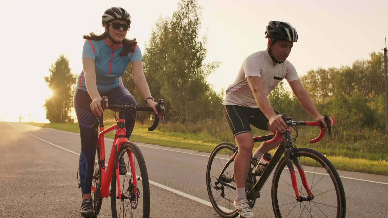 두 명의 건강한 여성과 여성이 해가 지는 도로 자전거를 타고 빠르게 이동하는 스테디캠