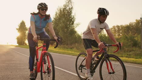 steadicam shot of two healthy mem and woman peddling fast with cycling road bicycle at sunset