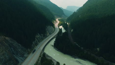 Cinematic-aerial-footage-tilting-up-and-revealing-the-breathtaking-view-of-the-kicking-horse-river-in-British-Columbia,-Canada-with-the-sun-lighting-parts-of-the-road-leading-through-the-valley