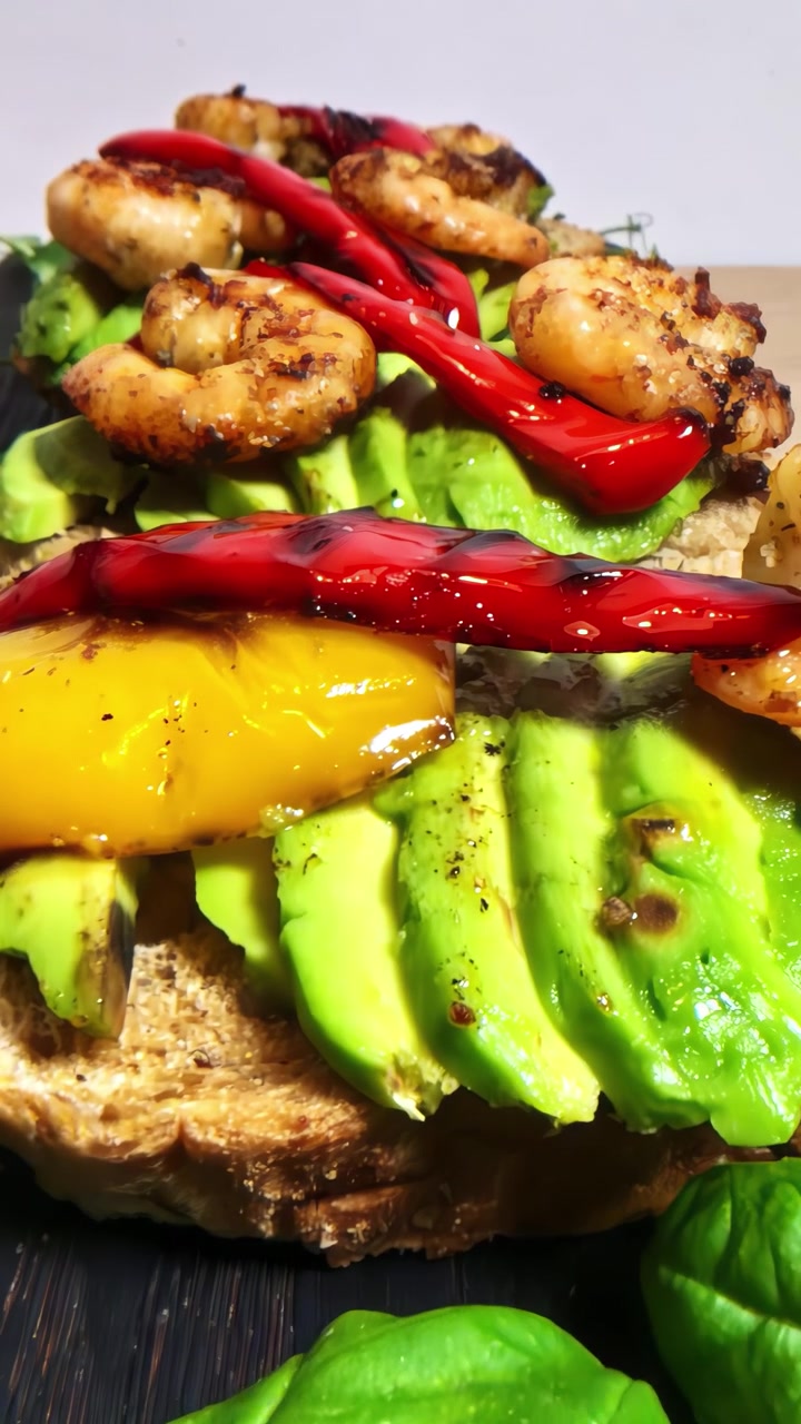 Gamberi grigliati e peperoni colorati su toast cremoso all'avocado, creando una vivace delizia culinaria.
