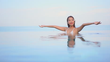 一个美丽的年轻女人从游泳池的水中高举她的手臂到天空的快乐