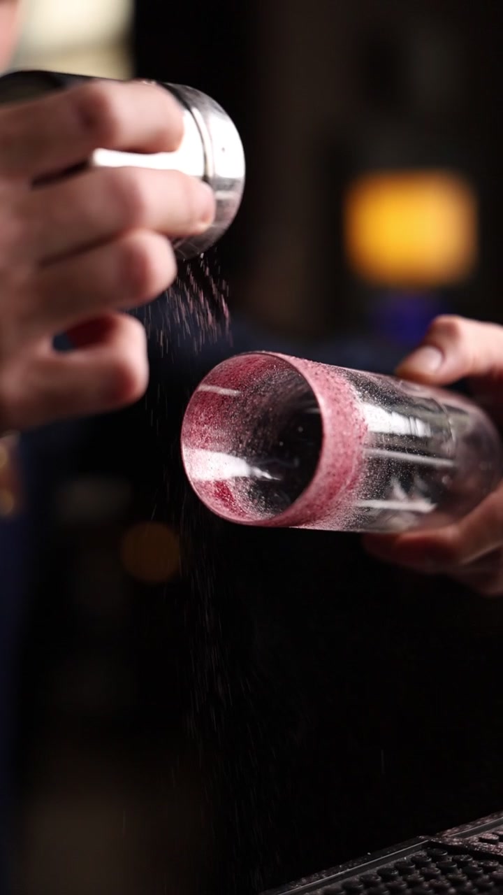 Barman che guarnisce un bicchiere da cocktail con un bordo di zucchero rosso