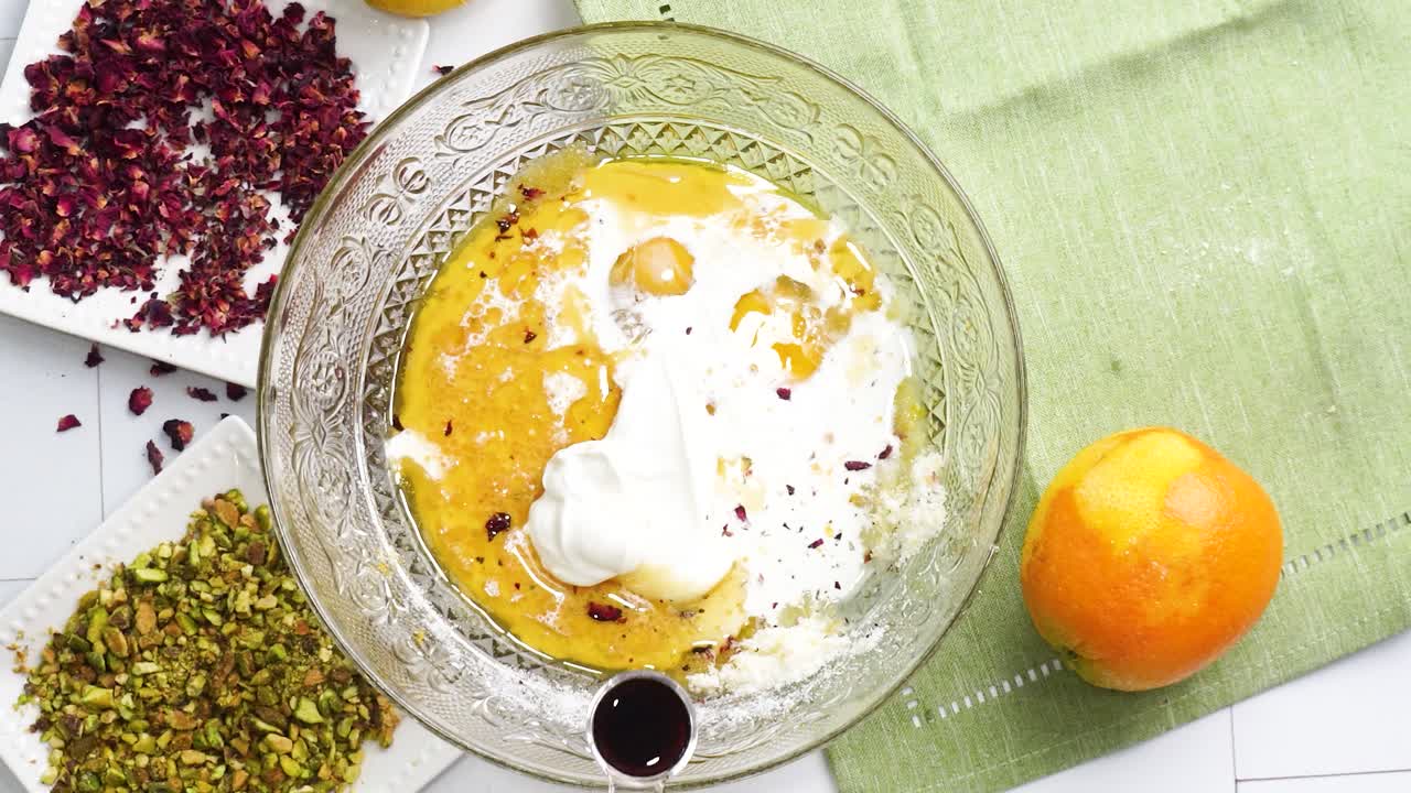 Baking a dessert called Persian Love Cake made with rose petals and pistachios. Cake with white glaze frosting. Mixing in the vanilla extract to the batter. Beautiful cake for tea time or celebration