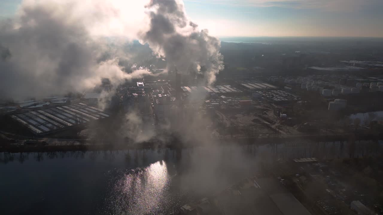 Industrial chimneys emitting white smoke over city skyline under blue sky, concept of pollution. Smooth aerial view flight overflight flyover drone
