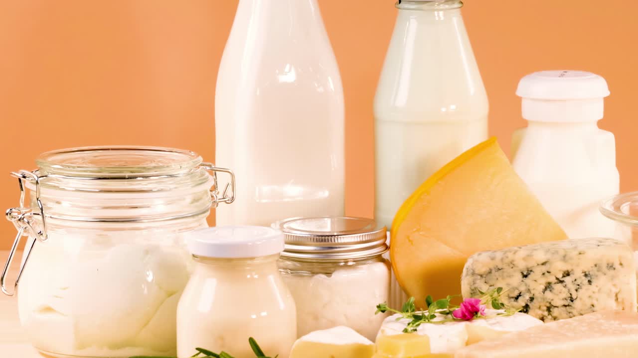 A selection of cheeses and dairy bottles arranged against an orange background, highlighting fresh ingredients.