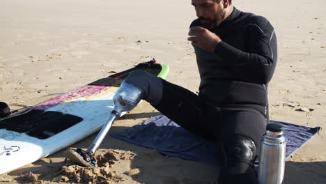 cámara lenta de un surfista masculino con pierna artificial bebiendo té en la playa