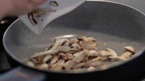 female chef pours sliced mushrooms in a frying pan