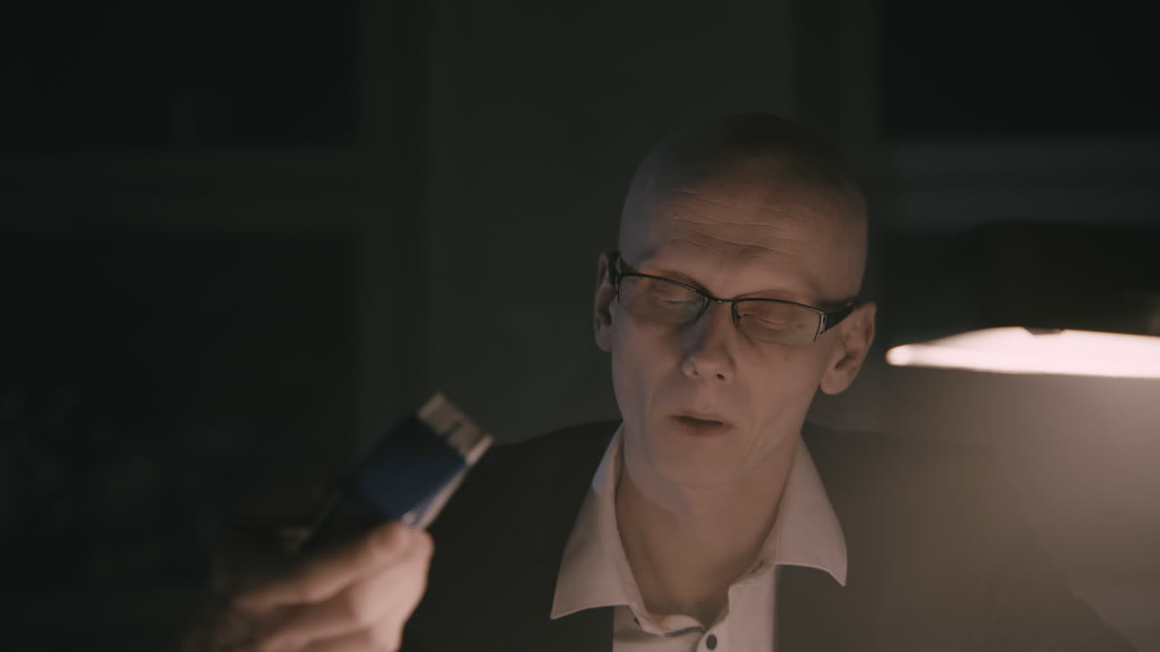 Pale bald accountant looks through the tax papers in the weird room at night