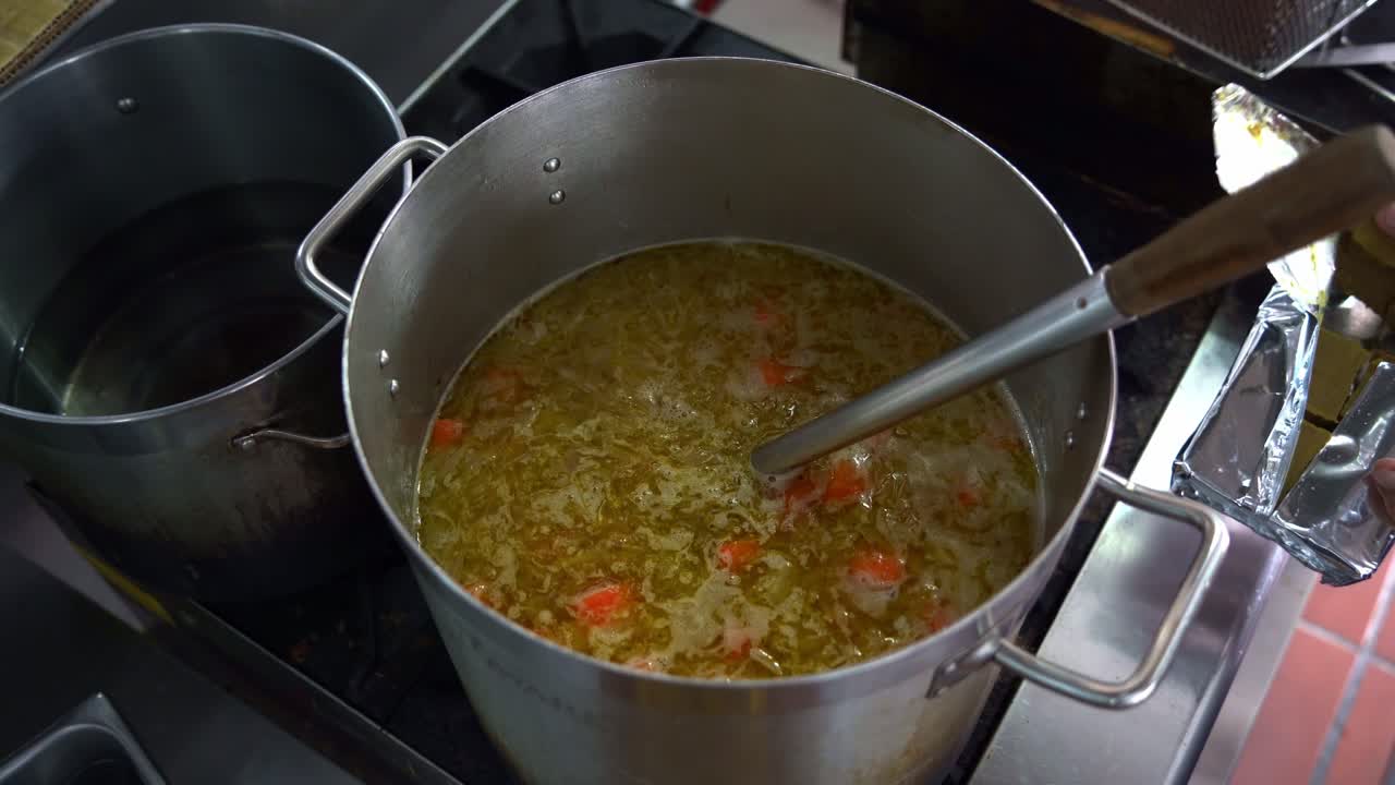 chef agregando bloques de curry roux japonés en una olla grande en la estufa, llena de papas, zanahorias y cebollas, vista de arriba hacia abajo