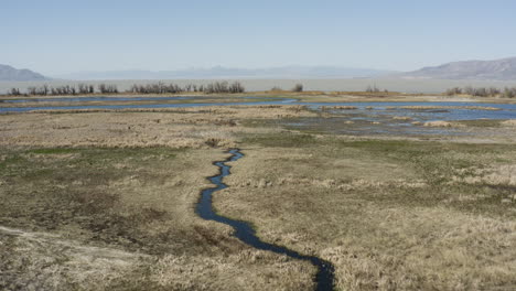 Reverse-drone-shot-overlooking-vast-wetlands-and-mountain-ranges-of-Powell-Slough,-Utah
