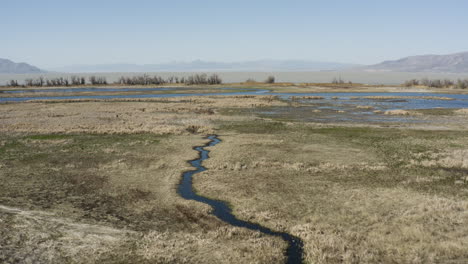 reverse drone shot overlooking vast wetlands and mountain ranges of powell slough, utah