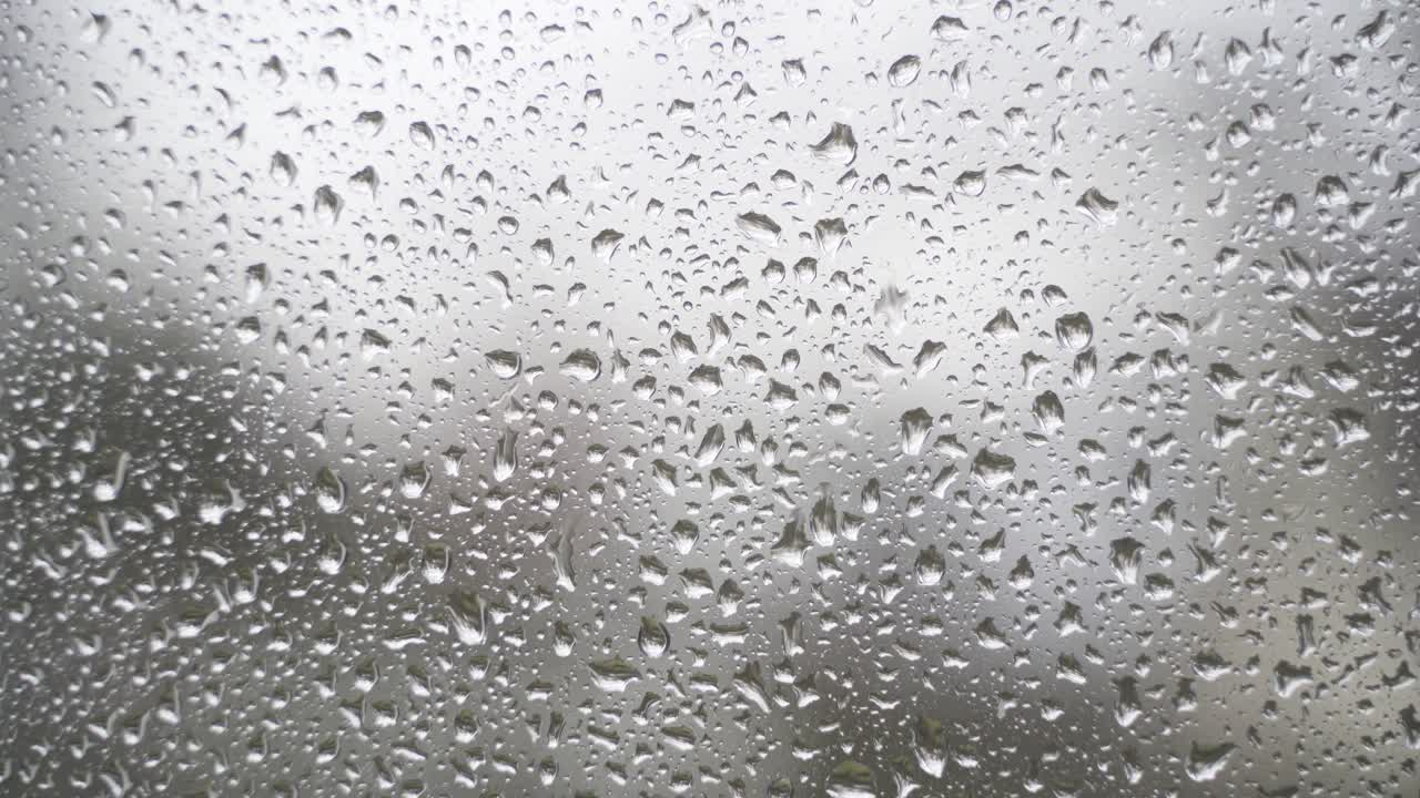 A steady 4k close-up of a window on a rainy day.
The small, aesthetic raindrops slowly run down the window pane.
