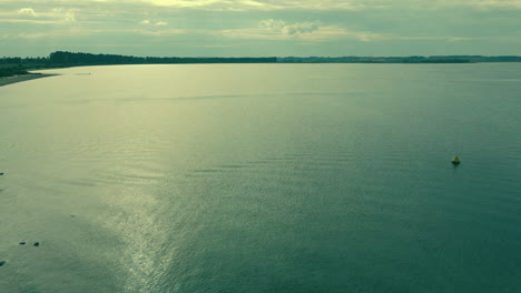 aerial-shot-low-waves-in-a-calm-sea-before-sunset,-near-coast-and-other-shore