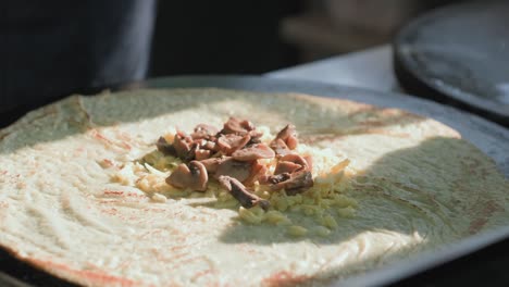 side view of cooking a russian pancake in a professional frying pan. the chef pours the dough into the pan and wraps the mushrooms and cheese in a baked pancake