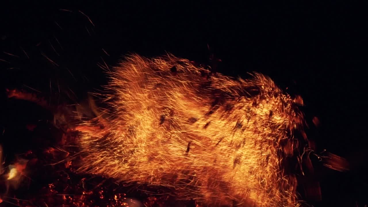 Flaming wood and flying sparks. Contrasting view of flaming logs against a black background. Fiery flame and smoke winding around the wooden remains