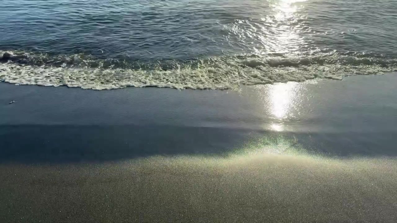 Ocean Waves Lapping on Black Sand Beach with Sunlight Reflection
