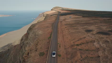 white car driving on a costal road on a cliff of la graciosa in spain with backdrop of the atlantic ocean