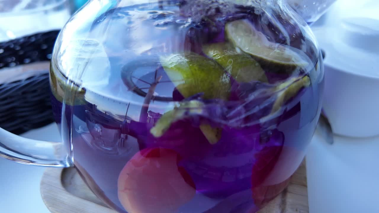 Close-up shot of a glass teapot filled with purple flower tea and lemon slices