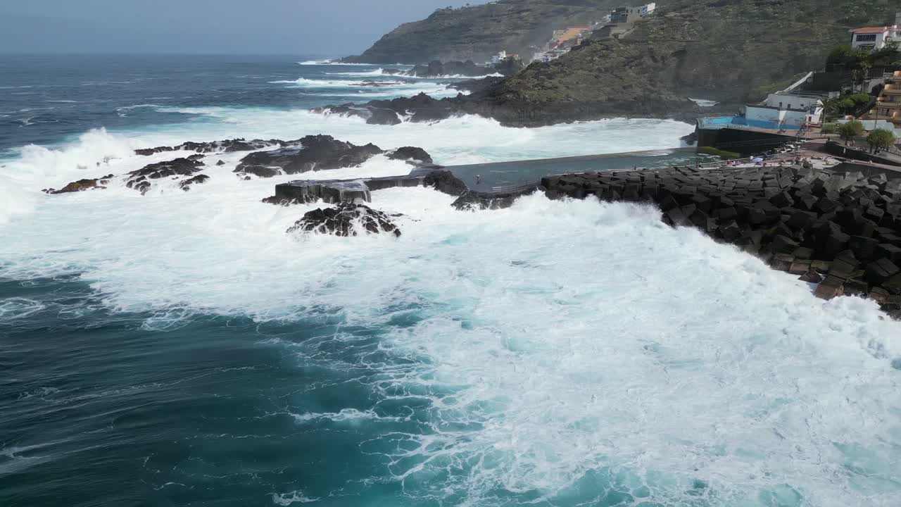 fuertes olas oceánicas golpeando bloques de barrera de hormigón en las piscinas de mesa del mar en tenerife islas canarias españa, toma aérea a la izquierda
