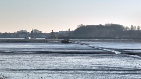 Low-orbiting-view-of-boardwalks-over-muddy-tidal-flats-early-in-the-morning-with-a-blue-cast-to-the-sky-and-a-ship-and-city-in-the-background