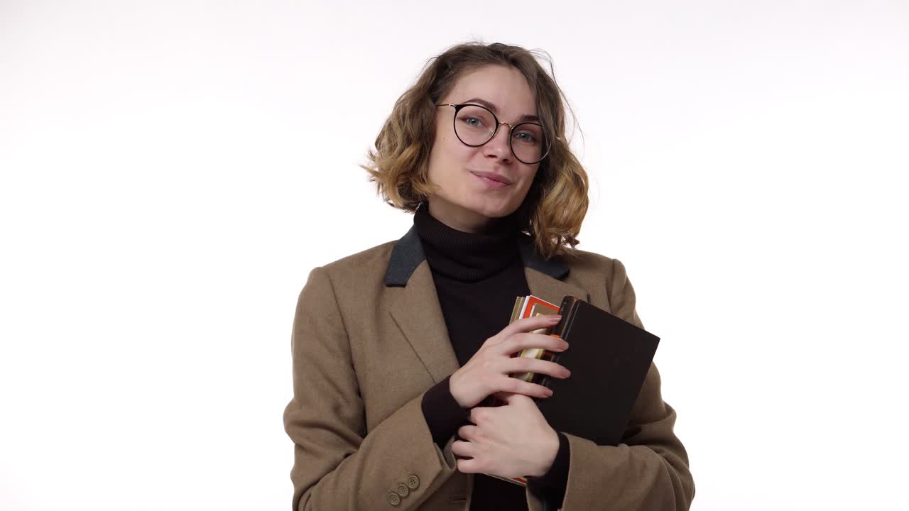 mujer estudiante de milenio sonriente sosteniendo libros y mirando a la cámara en fondo blanco. joven mujer europea con gafas elegantes estudiando en la universidad o empleado fresco