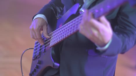 Close-up-of-a-professional-musician-in-a-black-suit-playing-on-an-electric-bass-guitar-during-a-live-session-on-stage-with-warm-studio-lights-in-the-blurred-background